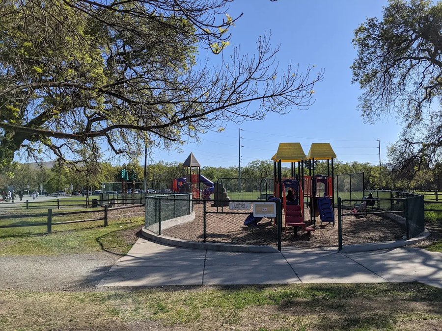 A large grassy area with trees and a playground at Newhall Community Park, The Crossings Community Concord, CA 94521.